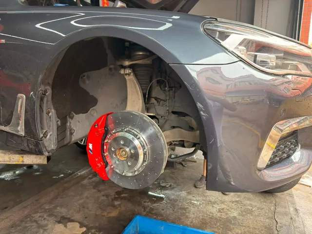 BMW 7 Series front corner in a workshop with its brake assembly exposed.