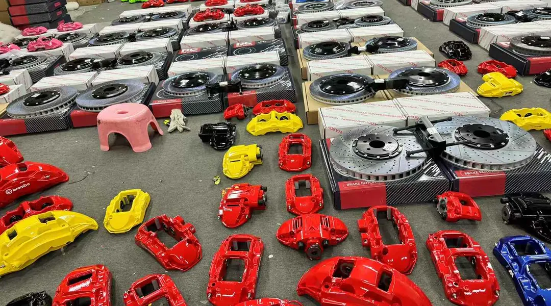 Rows of red, yellow, black and blue brake calipers after finishing, with brake discs staged on pallets