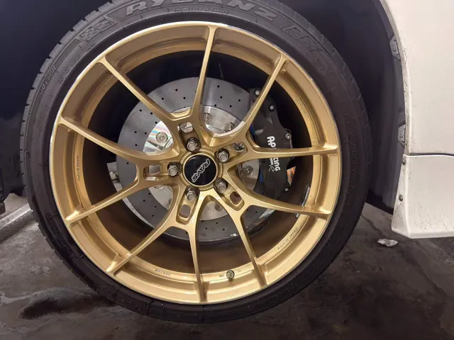 Black caliper and drilled rotor behind a gold wheel on a white Toyota Alphard