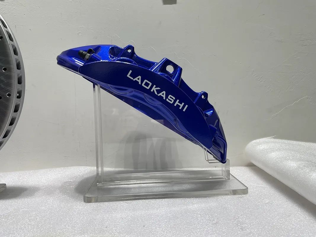 Close-up of a blue six-piston brake caliper showing its mounting ears and finish