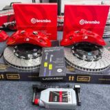 Technician checking front caliper clearance against the wheel spokes and inner barrel during fitment approval.