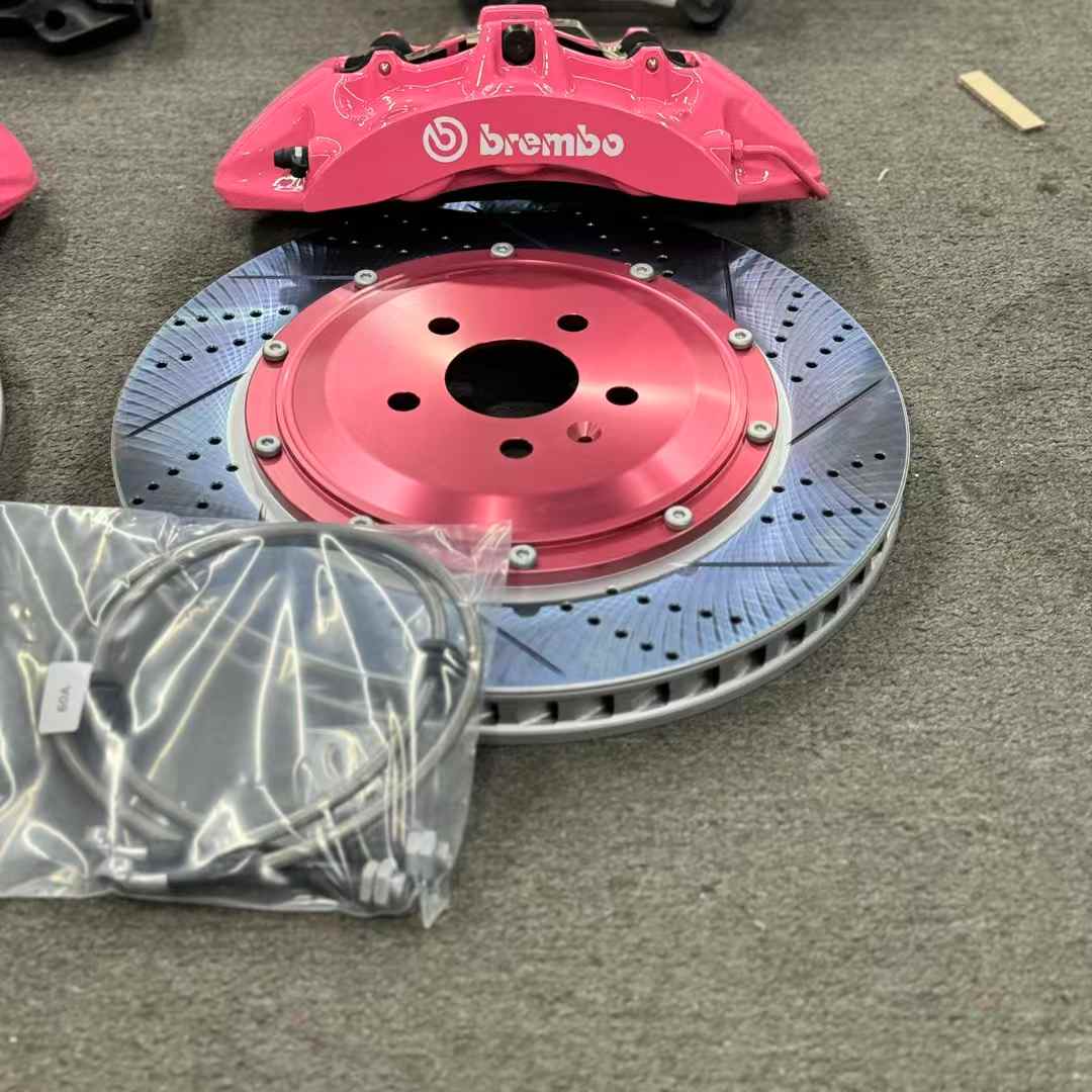 Drilled two-piece brake rotor with pink caliper and packaged brake hoses for component inspection