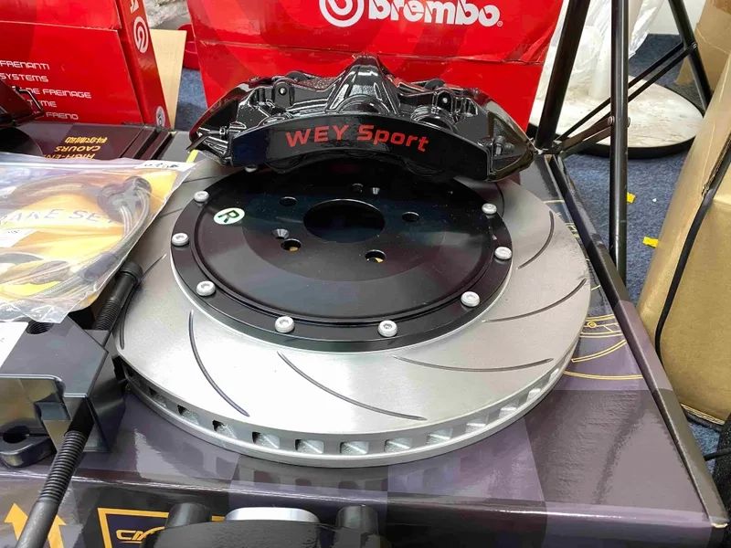 Close view of a black six-piston caliper positioned over a slotted ventilated two-piece rotor