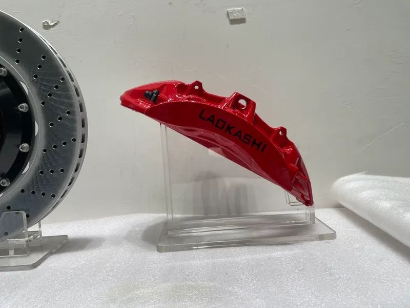 Red front brake caliper displayed separately with a drilled rotor at the side