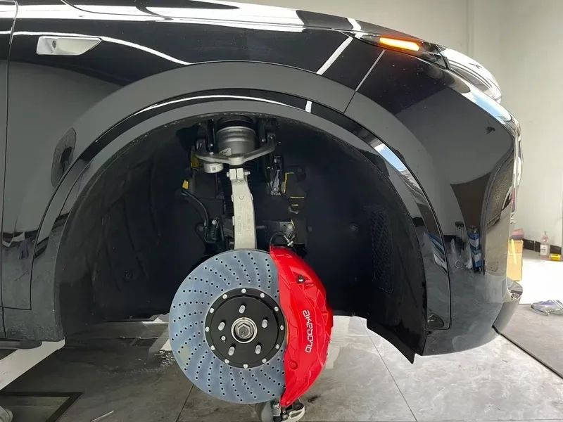 Black car with the front wheel removed showing a drilled rotor and a red brake caliper mounted on the hub