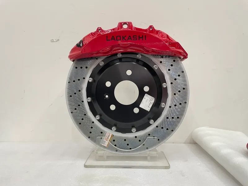 Red front brake caliper positioned over a drilled rotor for component layout reference